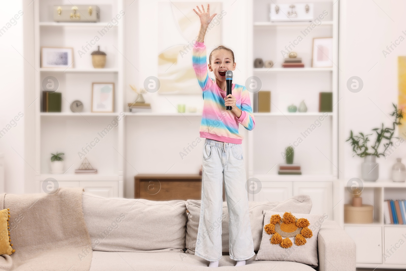 Photo of Little girl with microphone singing on sofa at home