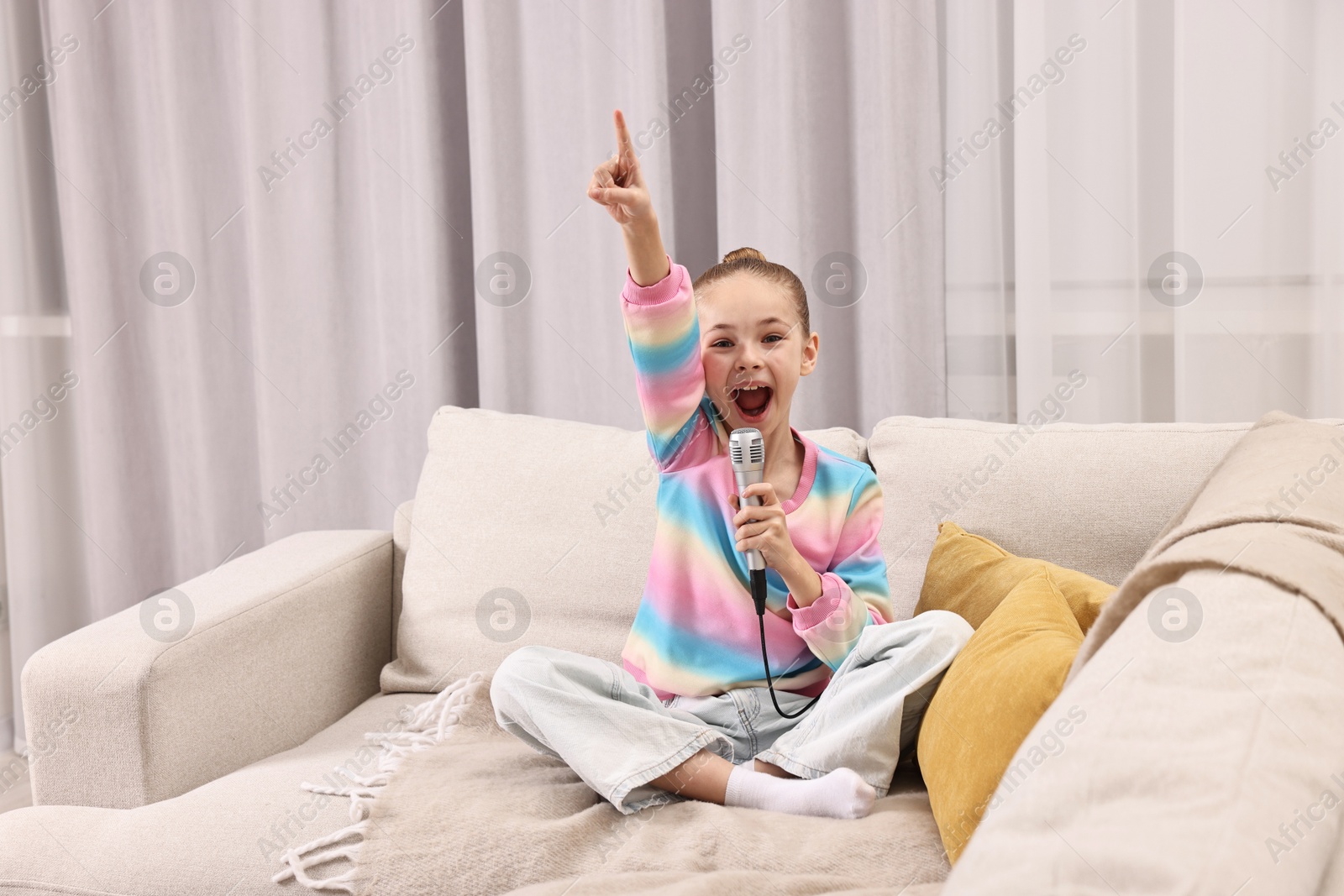 Photo of Little girl with microphone singing on sofa at home