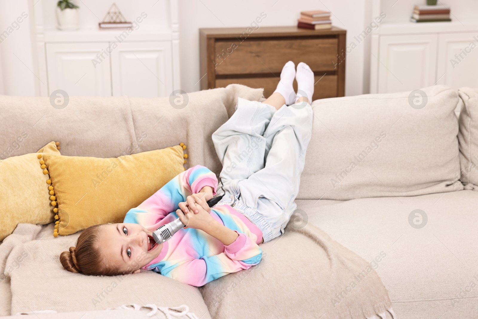 Photo of Little girl with microphone singing on sofa at home