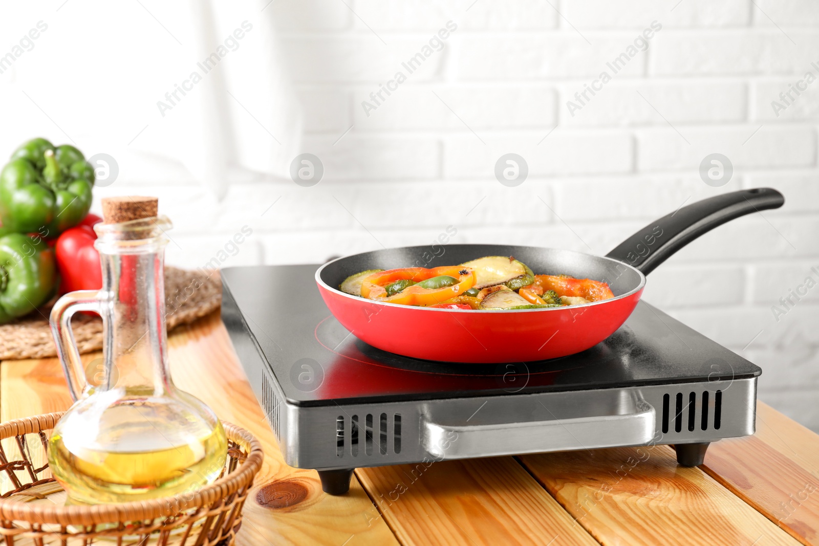 Photo of Frying pan with vegetables, stove and oil on wooden table indoors