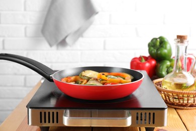 Photo of Frying pan with vegetables and stove on wooden table indoors, closeup