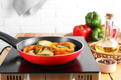 Photo of Frying pan with vegetables and stove on wooden table indoors, closeup