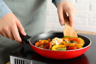 Photo of Woman frying vegetables in pan on stove at table indoors, closeup