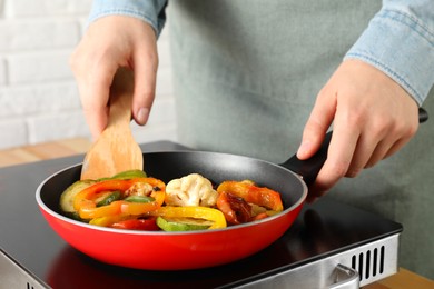 Photo of Woman frying vegetables in pan on stove at table indoors, closeup