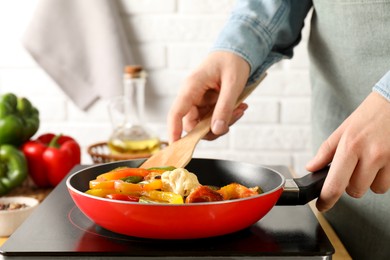 Photo of Woman frying vegetables in pan on stove at table indoors, closeup