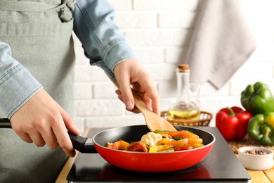 Photo of Woman frying vegetables in pan on stove at table indoors, closeup