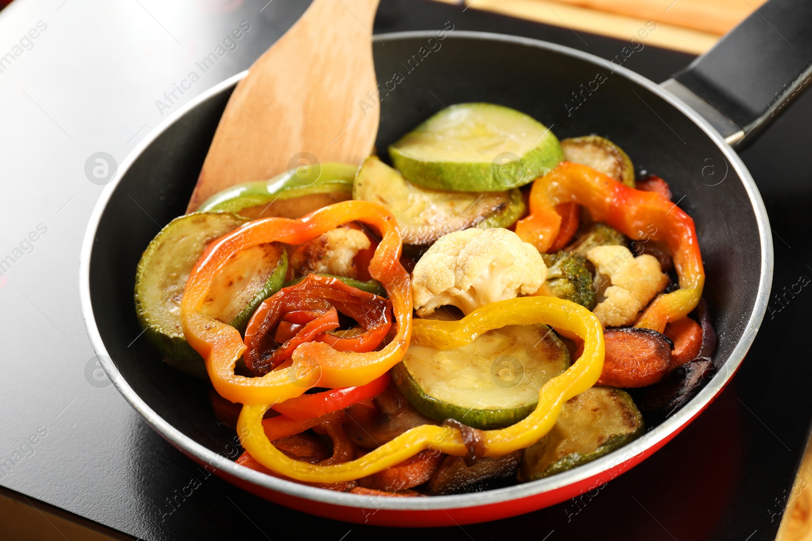 Photo of Frying pan with vegetables and stove on table, closeup