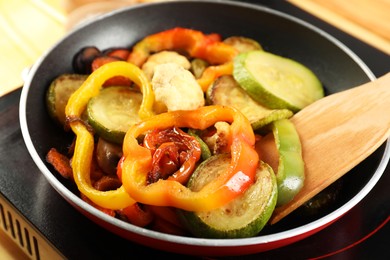 Photo of Frying pan with vegetables and stove on table, closeup