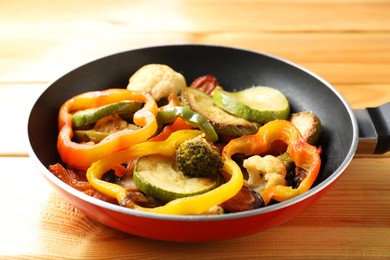 Photo of Frying pan with vegetables on wooden table, closeup