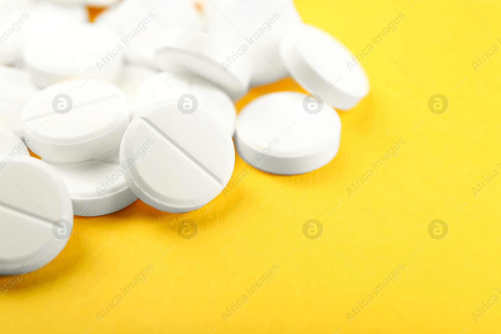 Photo of Pile of antibiotic pills on yellow background, closeup