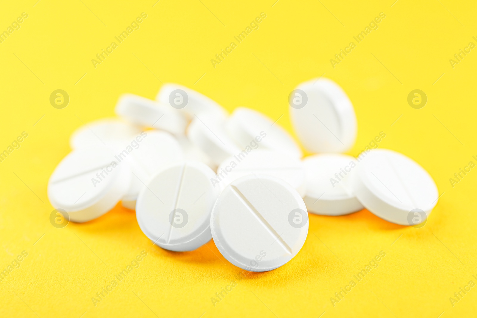 Photo of Pile of antibiotic pills on yellow background, closeup