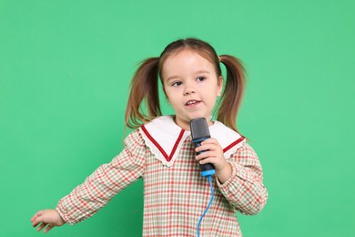 Photo of Cute girl with microphone singing on green background