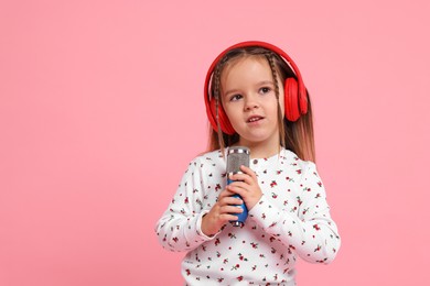 Photo of Cute girl with microphone and headphones singing on pink background. Space for text