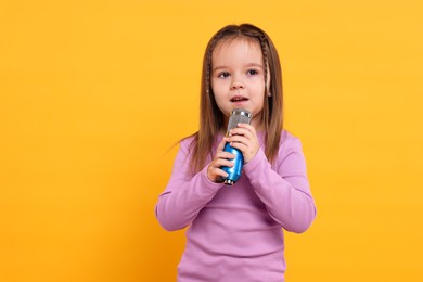 Photo of Cute girl with microphone singing on orange background