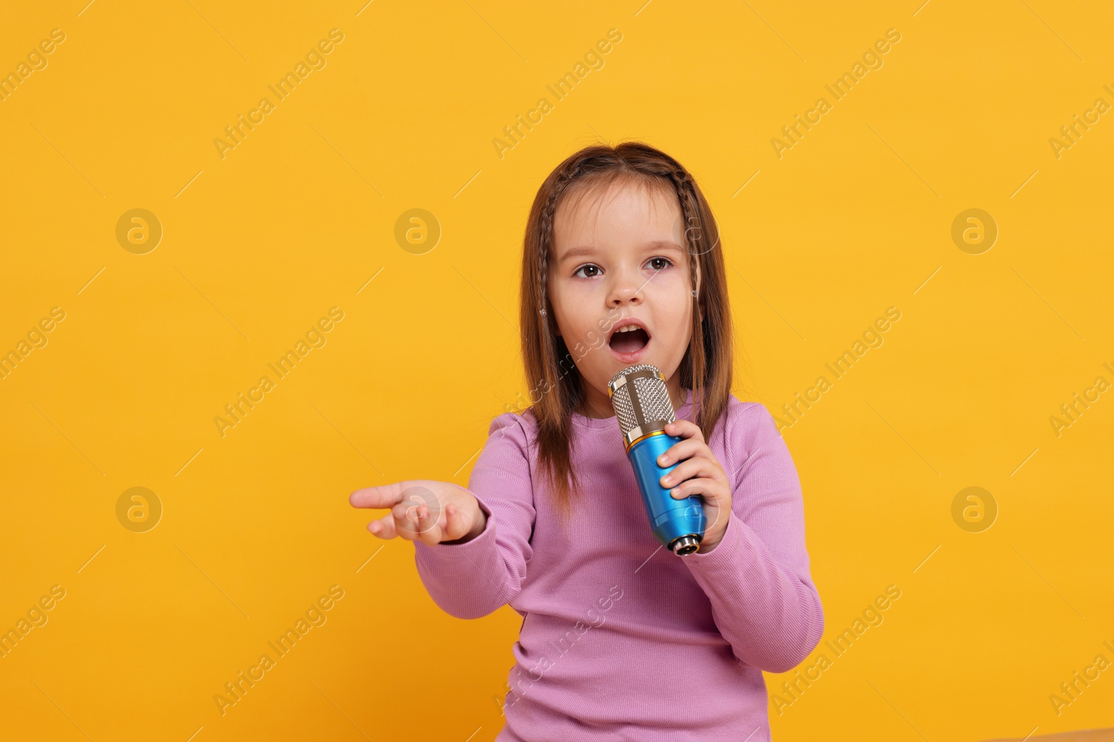 Photo of Cute girl with microphone singing on orange background