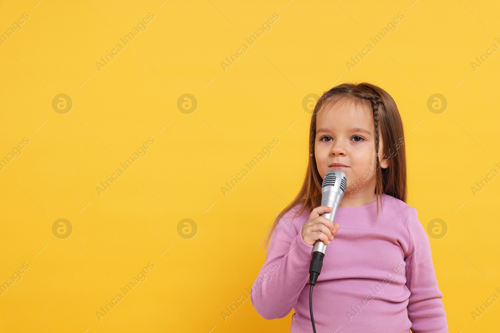 Photo of Cute girl with microphone on orange background. Space for text