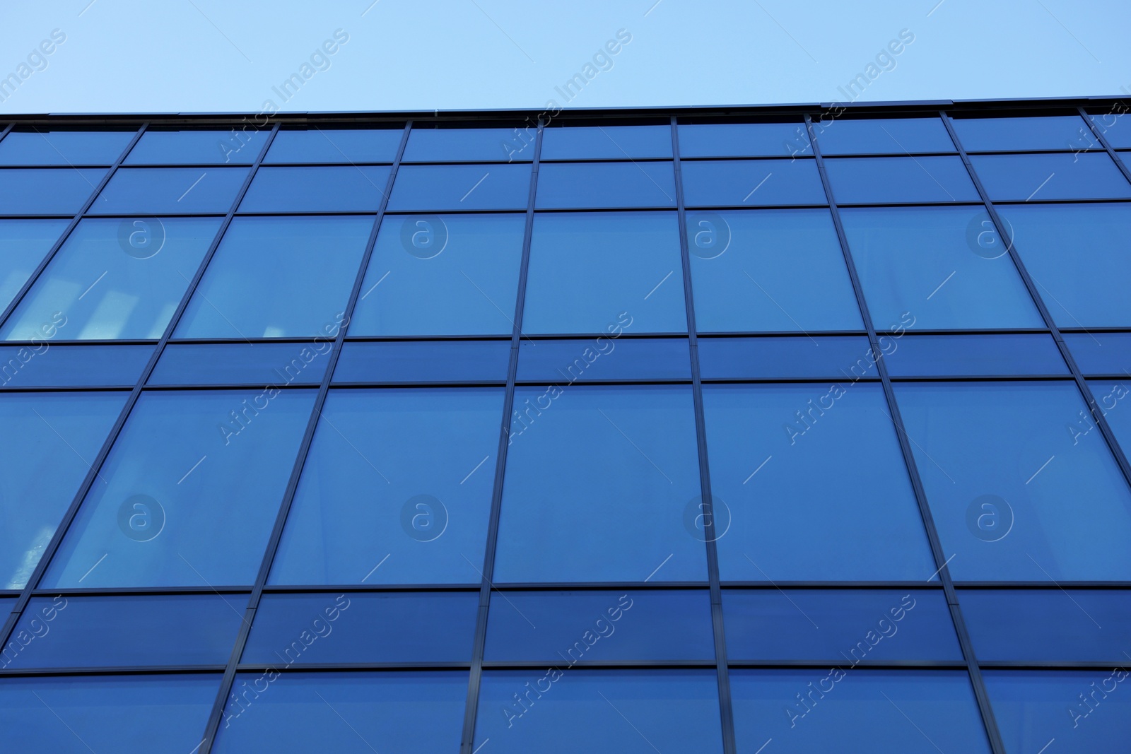 Photo of Exterior of modern building with many windows against light blue sky, low angle view