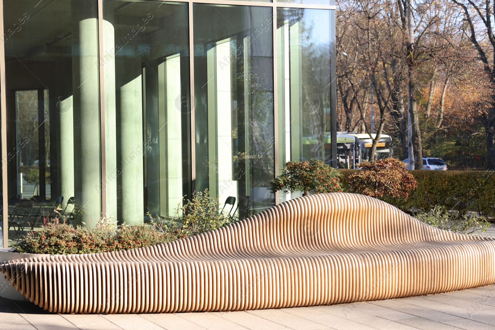 Photo of Modern building with many windows and wooden bench in city