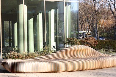 Photo of Modern building with many windows and wooden bench in city