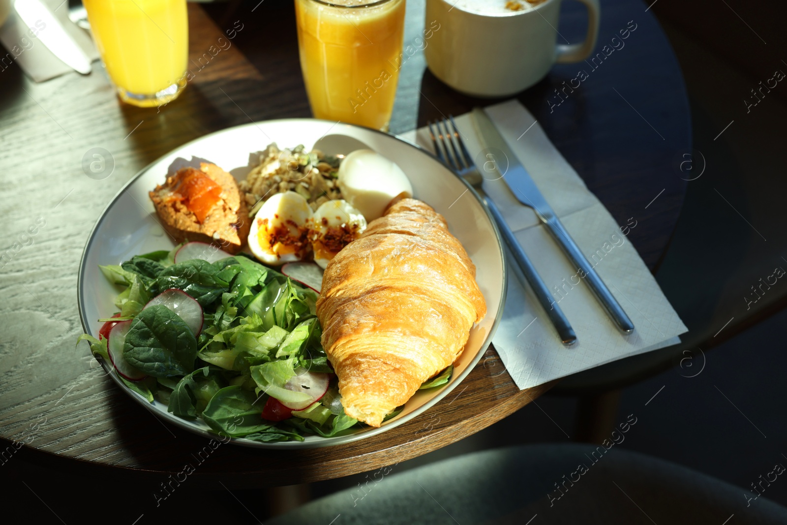 Photo of Tasty breakfast. Freshly baked croissant and salad served on wooden table in cafe, closeup