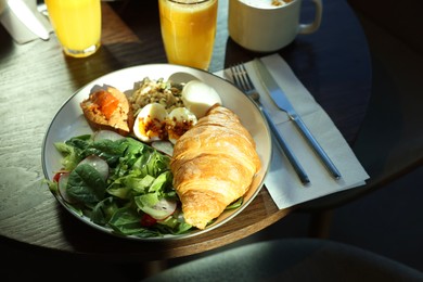 Photo of Tasty breakfast. Freshly baked croissant and salad served on wooden table in cafe, closeup