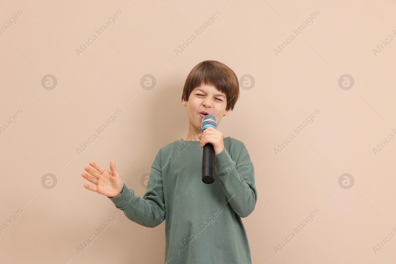 Photo of Cute boy with microphone singing near beige wall