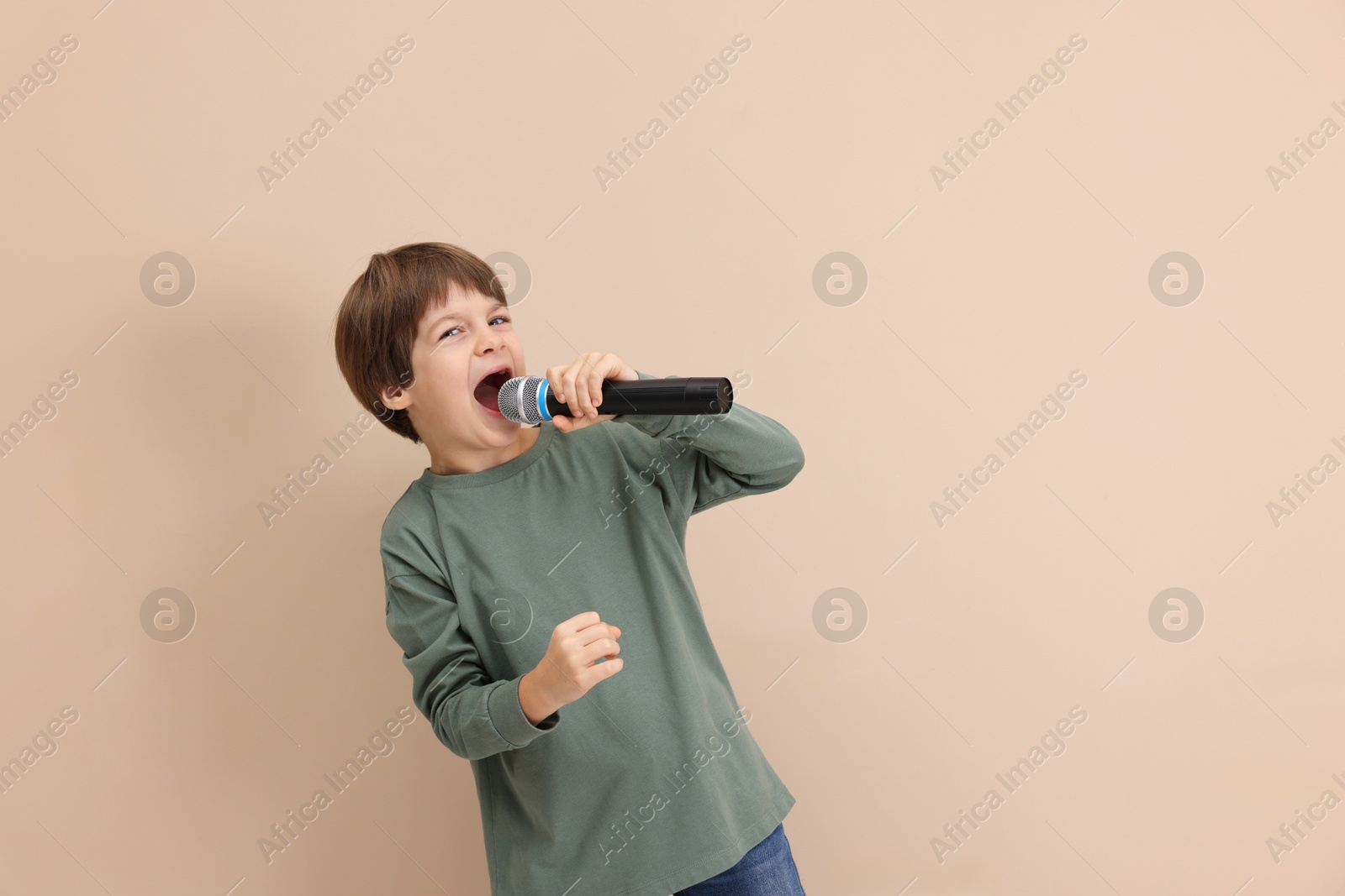 Photo of Cute boy with microphone singing near beige wall