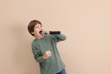 Photo of Cute boy with microphone singing near beige wall