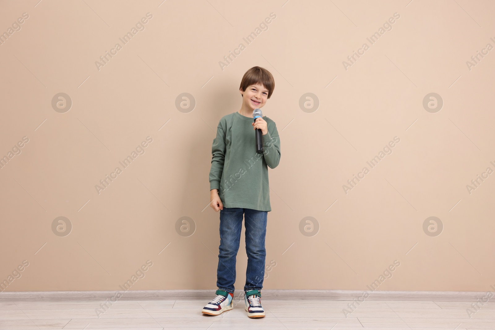 Photo of Smiling boy with microphone near beige wall