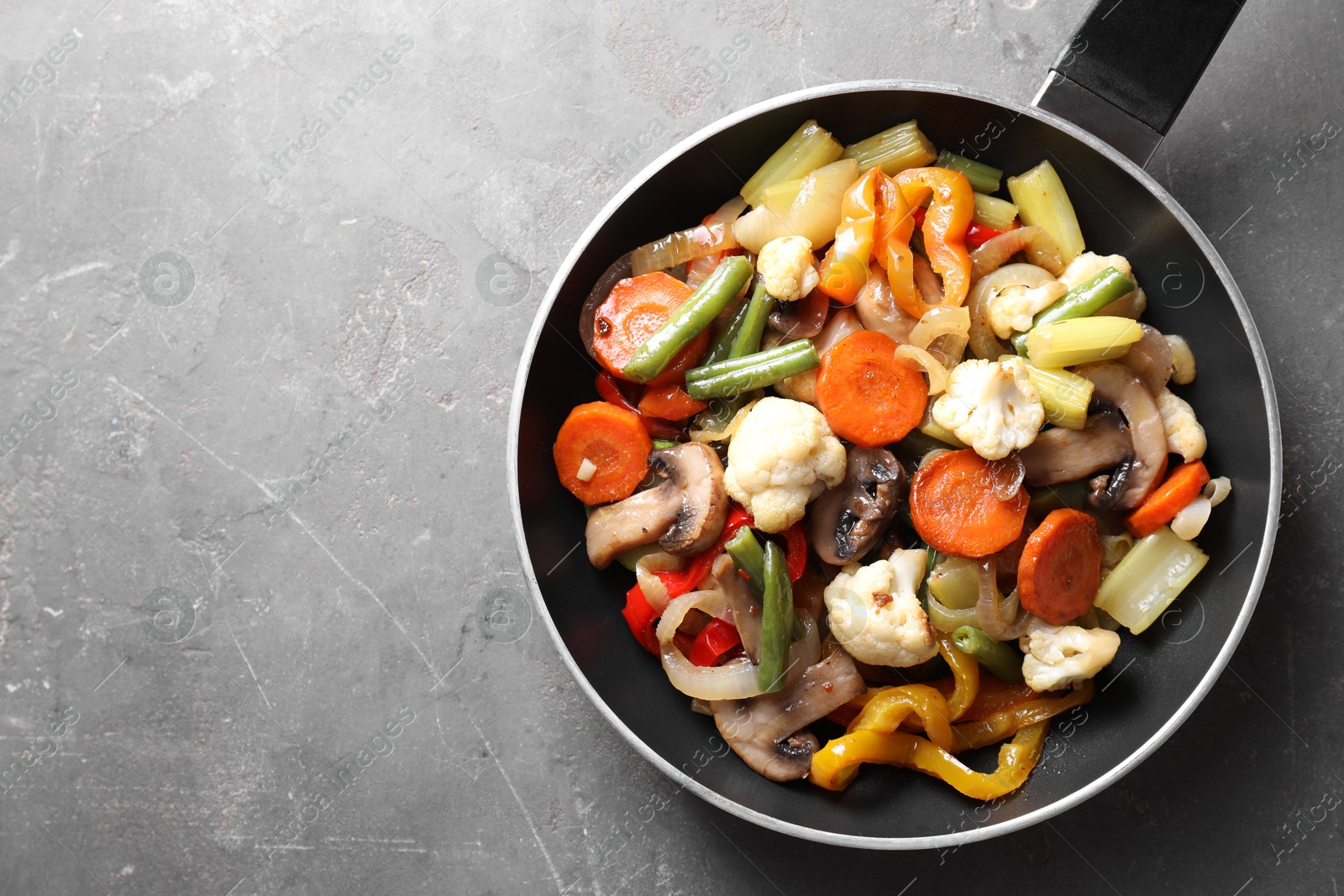 Photo of Different vegetables and mushrooms in frying pan on grey table, top view. Space for text