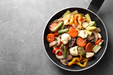 Photo of Different vegetables and mushrooms in frying pan on grey table, top view. Space for text