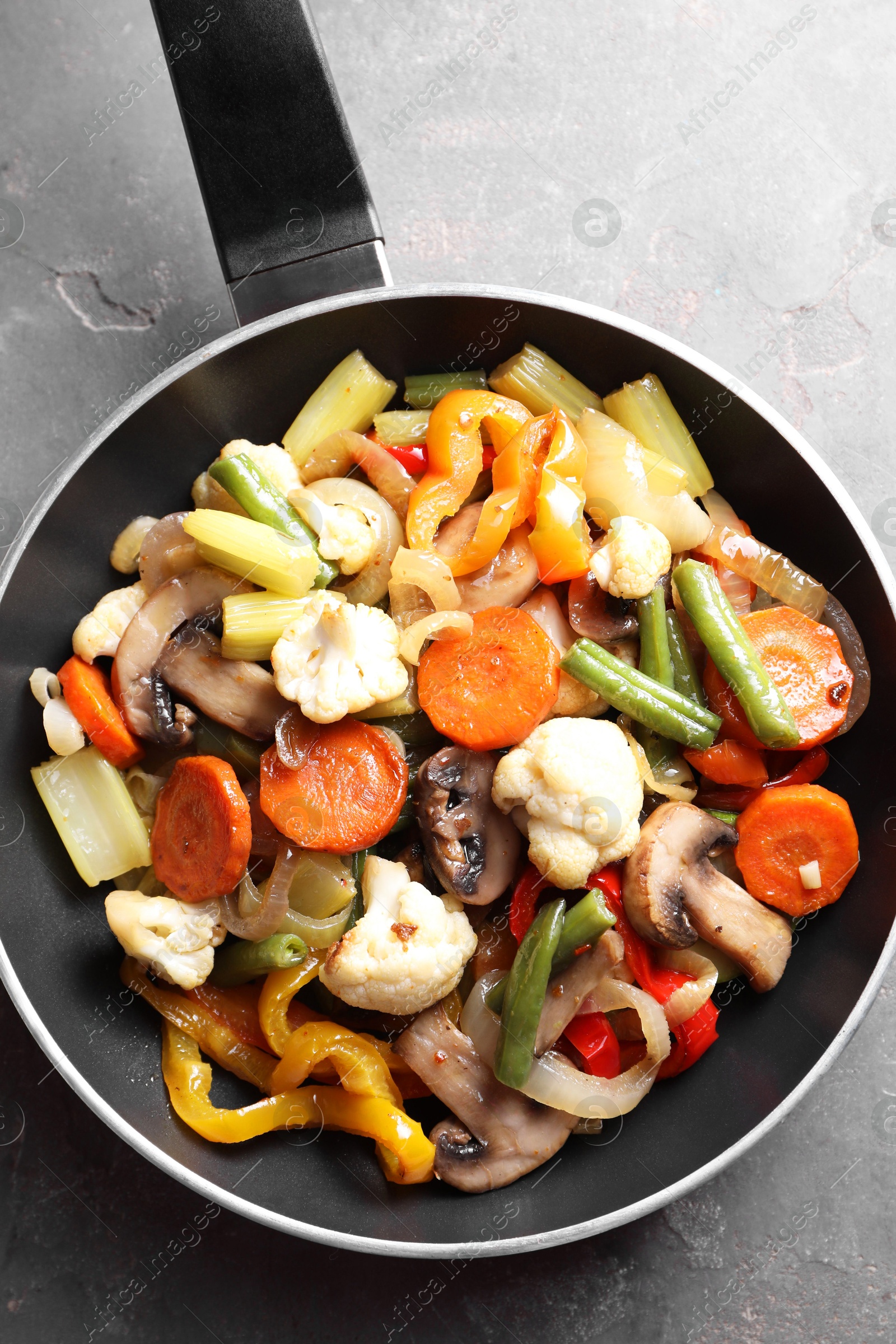 Photo of Different vegetables and mushrooms in frying pan on grey table, top view