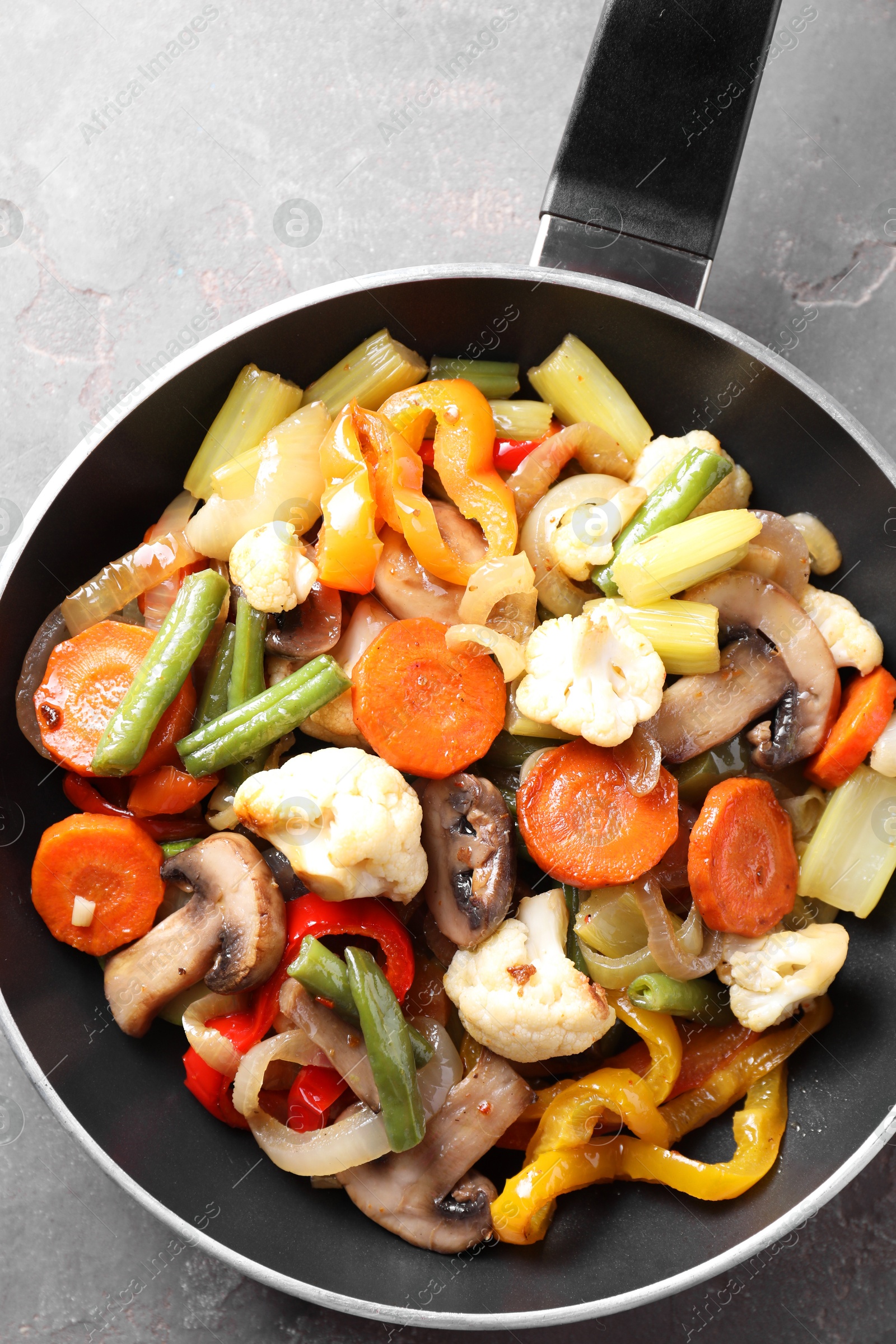 Photo of Different vegetables and mushrooms in frying pan on grey table, top view