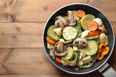 Photo of Different vegetables and mushrooms in frying pan on wooden table, top view. Space for text