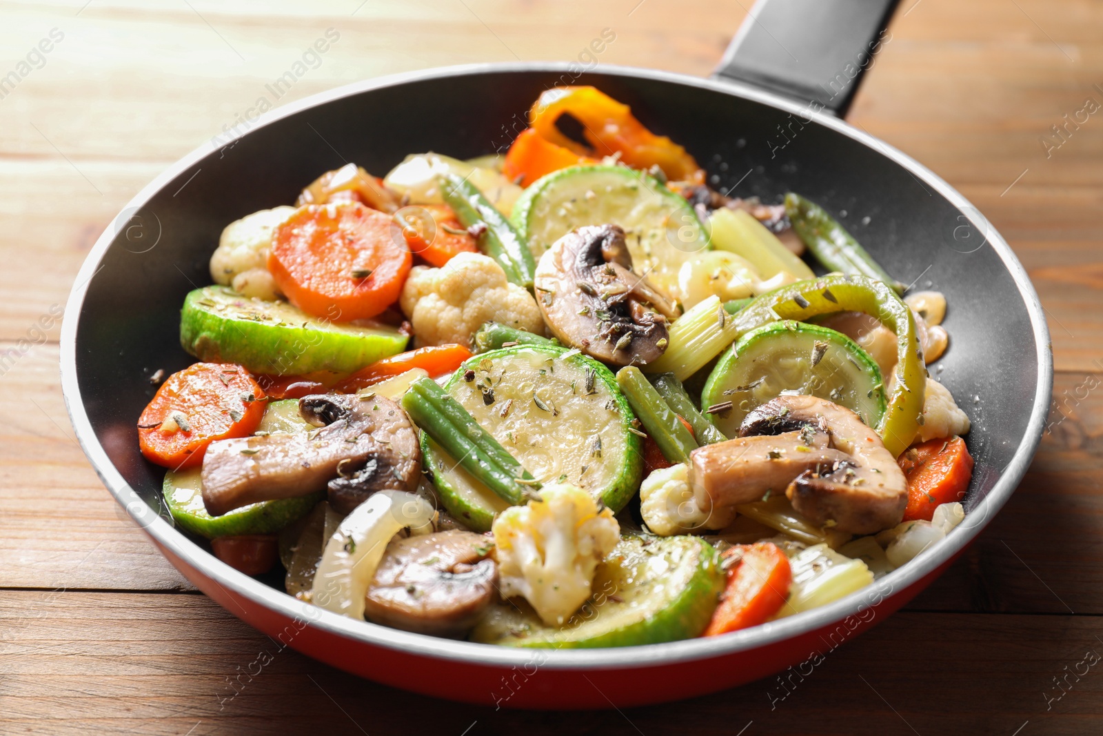 Photo of Different vegetables and mushrooms in frying pan on wooden table, closeup