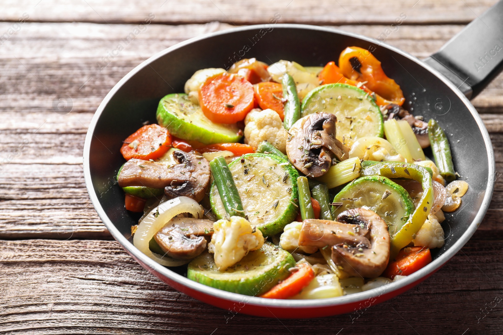 Photo of Different vegetables and mushrooms in frying pan on wooden table, closeup