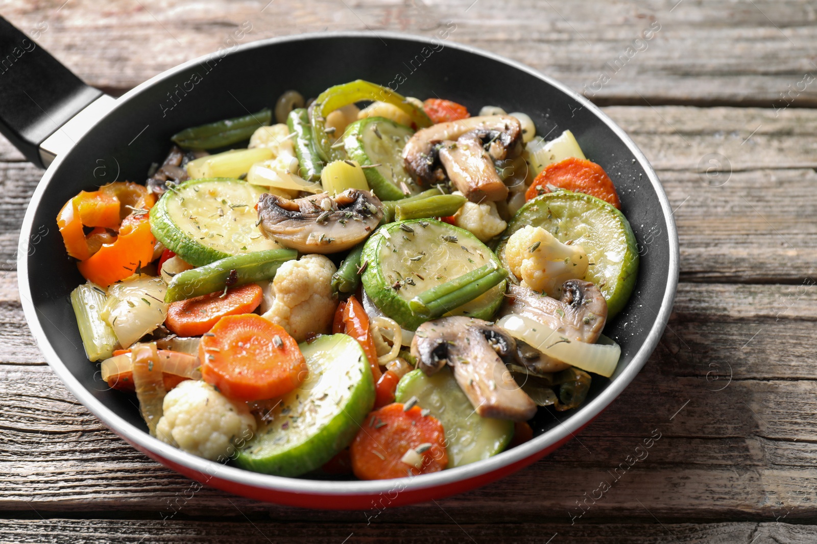 Photo of Different vegetables and mushrooms in frying pan on wooden table, closeup