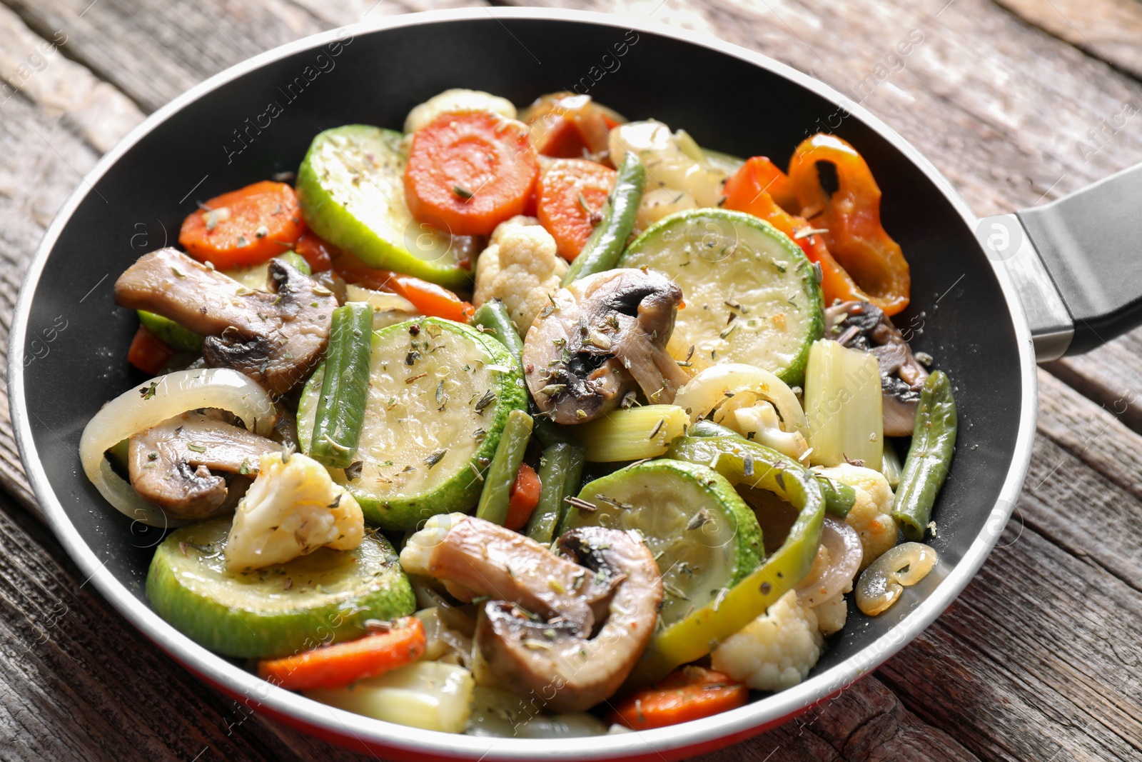 Photo of Different vegetables and mushrooms in frying pan on wooden table, closeup