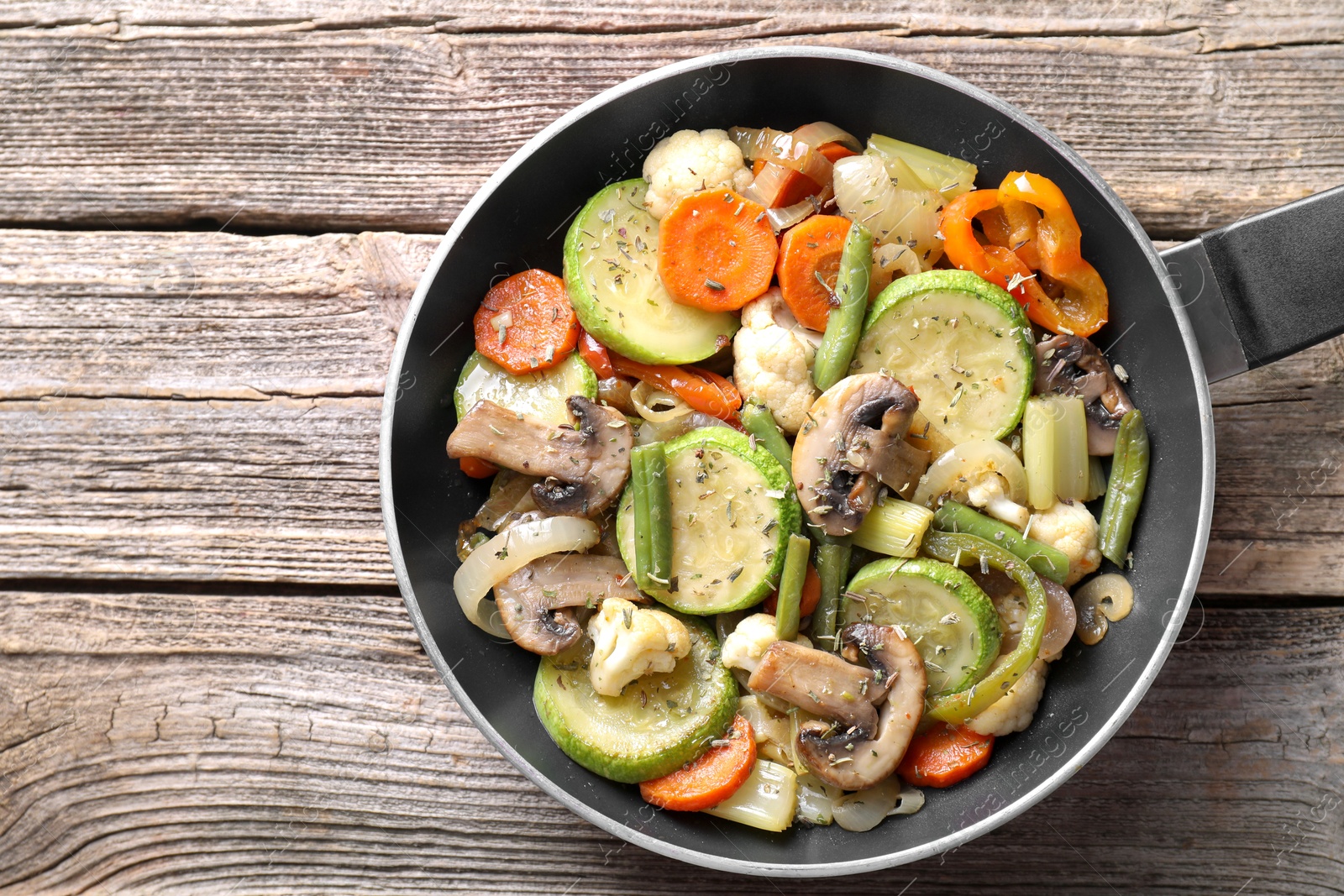 Photo of Different vegetables and mushrooms in frying pan on wooden table, top view