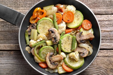 Photo of Different vegetables and mushrooms in frying pan on wooden table, top view