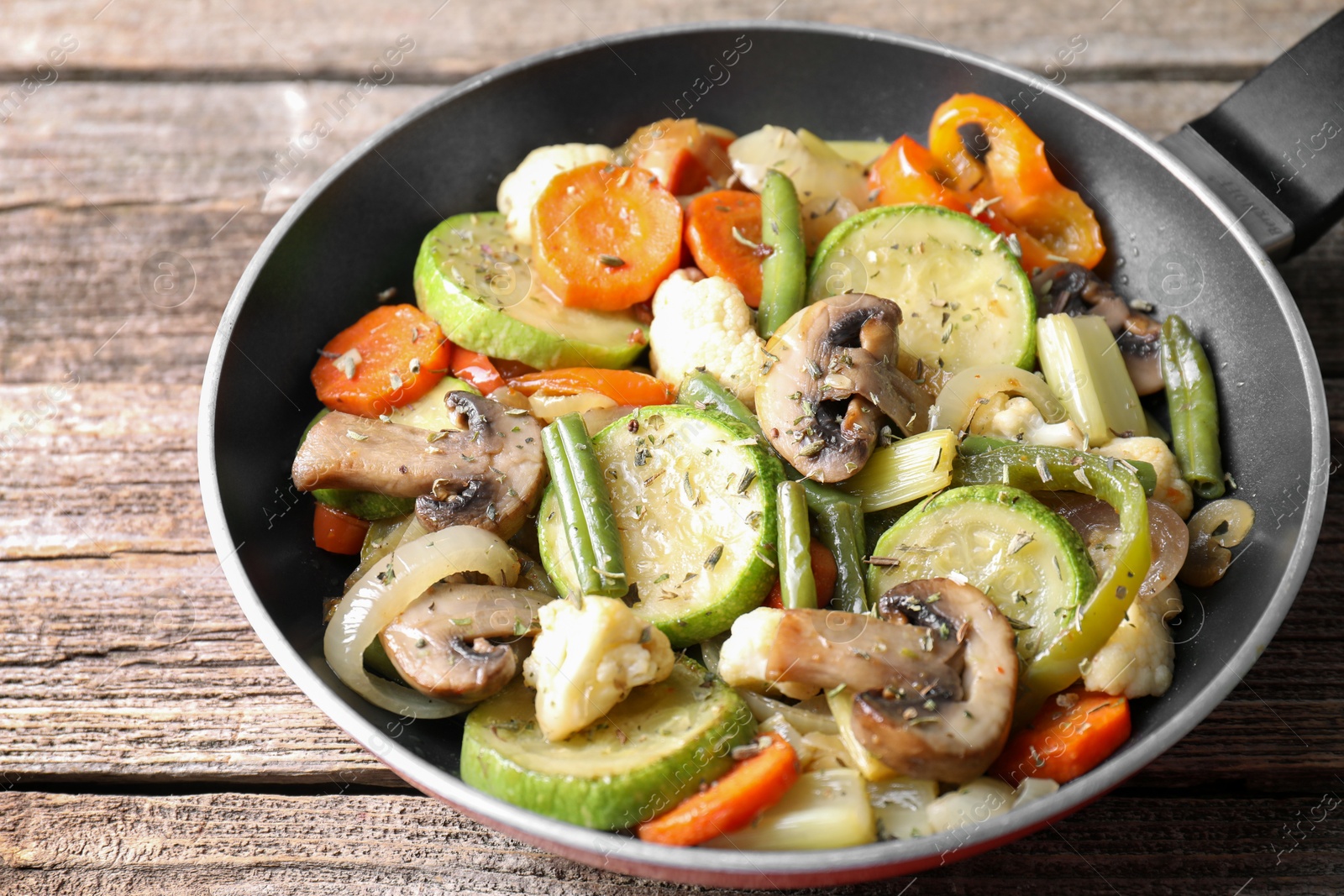 Photo of Different vegetables and mushrooms in frying pan on wooden table, closeup