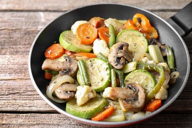 Photo of Different vegetables and mushrooms in frying pan on wooden table, closeup