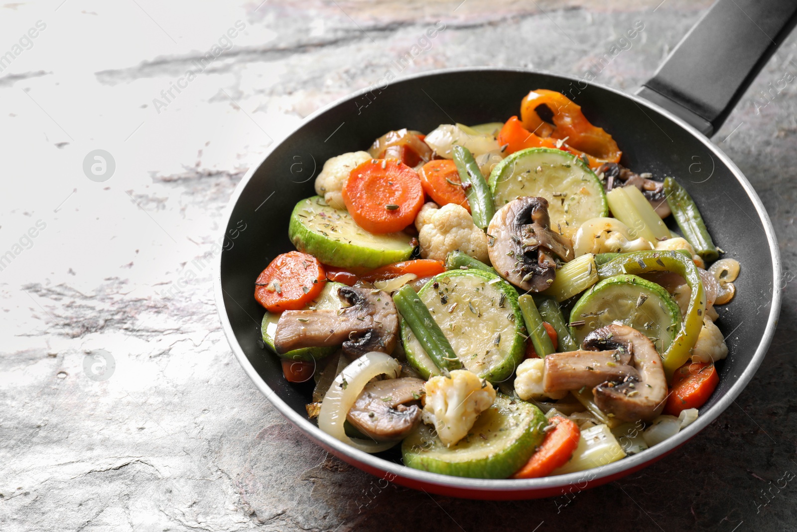 Photo of Different vegetables and mushrooms in frying pan on grey textured table, closeup