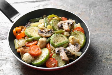 Photo of Different vegetables and mushrooms in frying pan on grey textured table, closeup