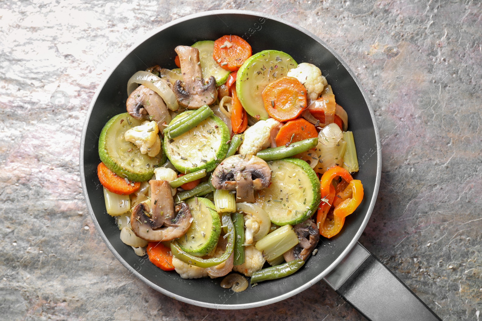 Photo of Different vegetables and mushrooms in frying pan on grey textured table, top view