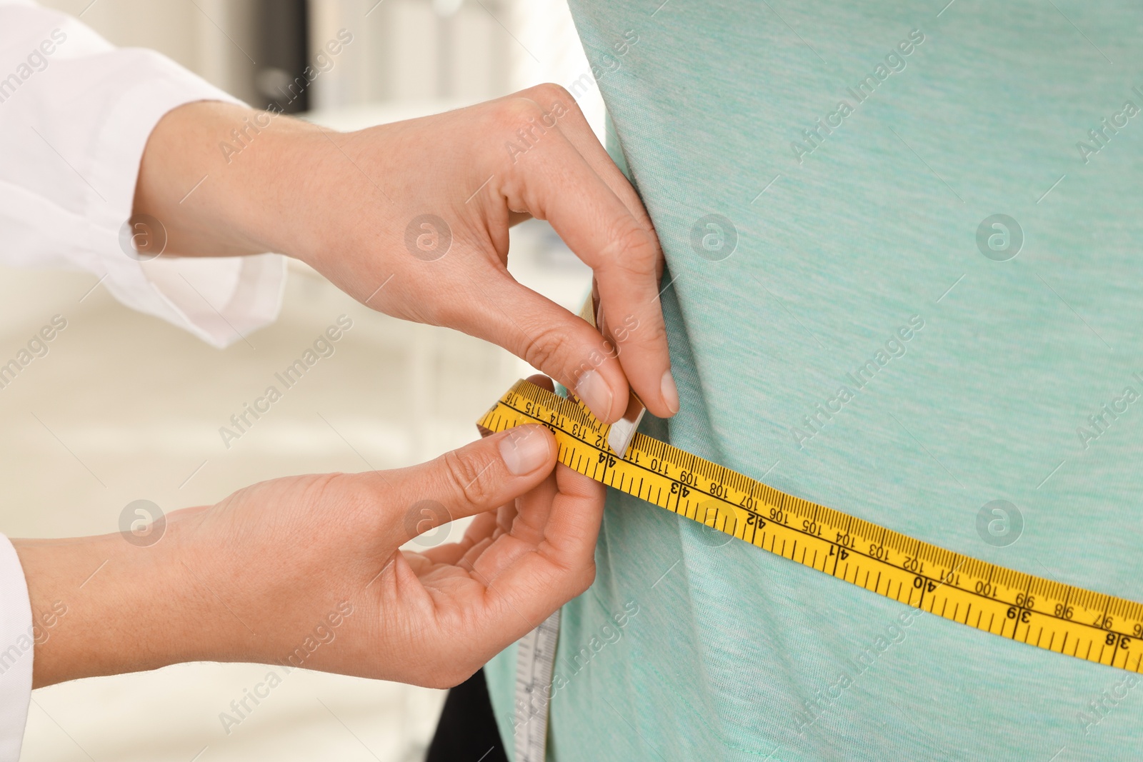 Photo of Nutritionist measuring overweight woman's waist with tape in hospital, closeup