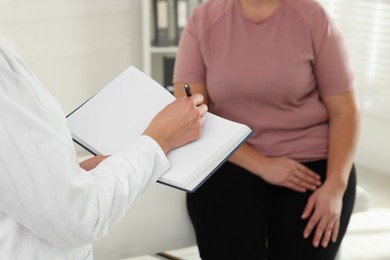 Photo of Nutritionist with notebook giving recommendations to overweight woman in hospital, closeup