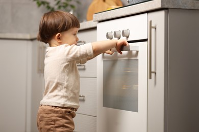 Photo of Little boy playing with oven in kitchen. Dangerous situation