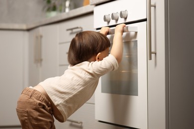 Photo of Little boy playing with oven in kitchen. Dangerous situation