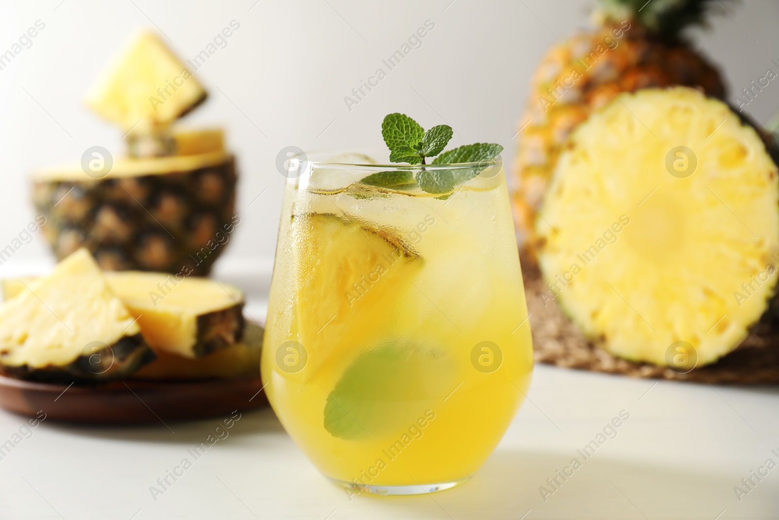 Photo of Tasty pineapple cocktail with mint in glass on light table, closeup